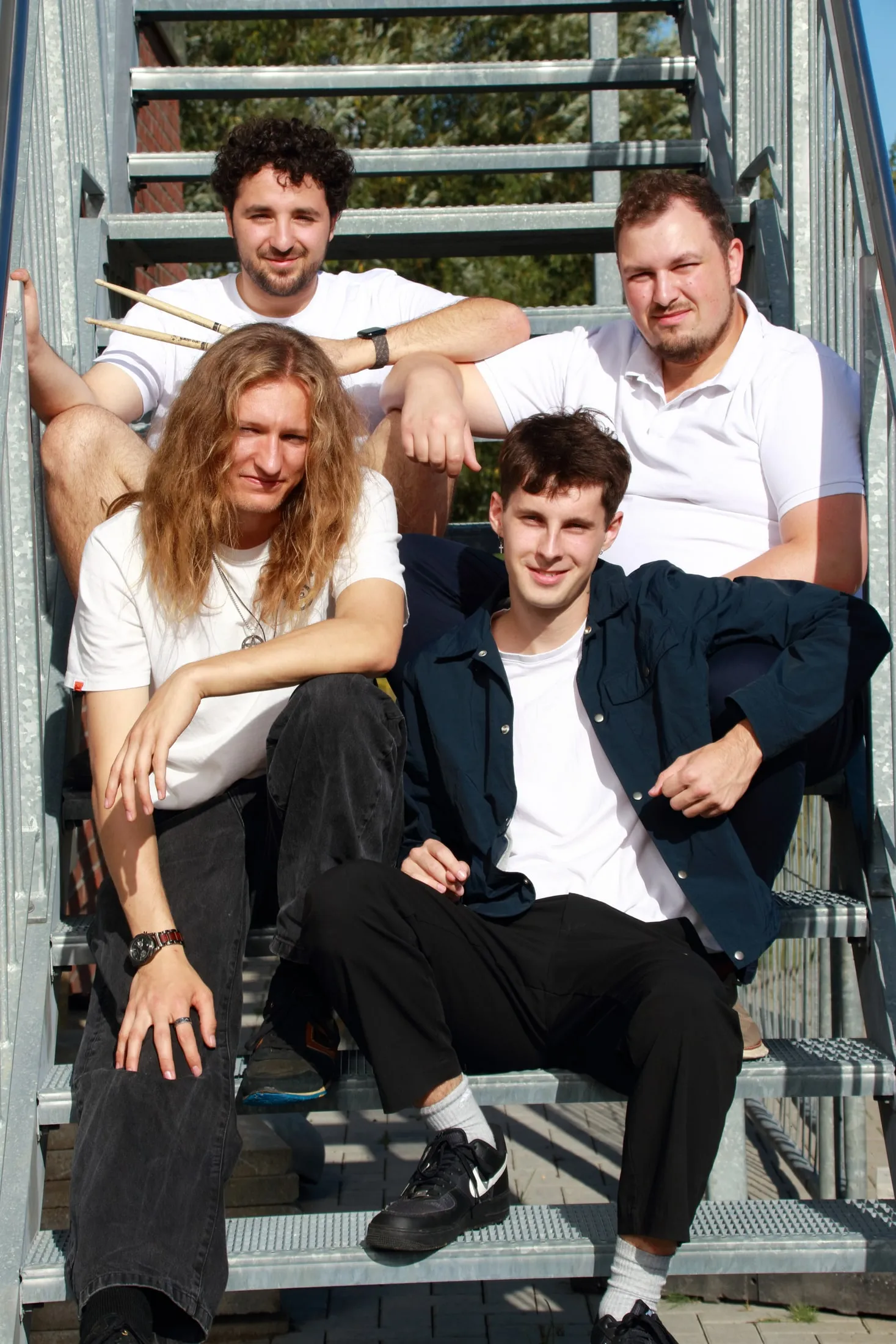 Die vier Bandmitglieder sitzen entspannt auf einer Metalltreppe