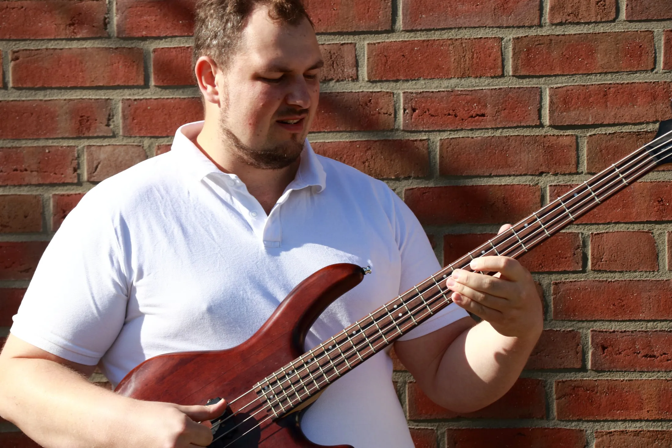 Bassist mit fünfsaitigem Bass vor einer Backsteinwand