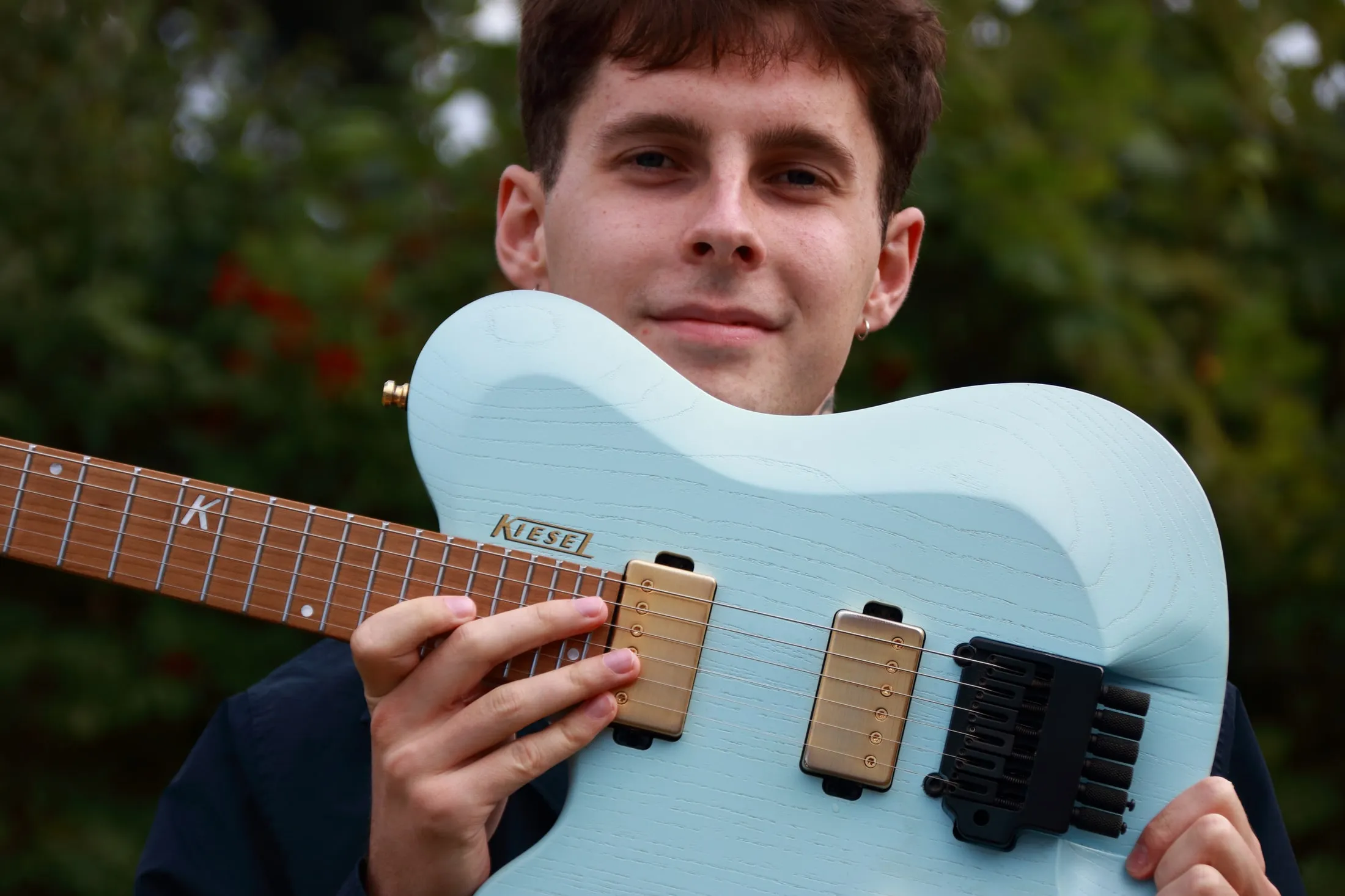 Ein Bandmitglied hält seine hellblaue E-Gitarre vor sich und lächelt in die Kamera