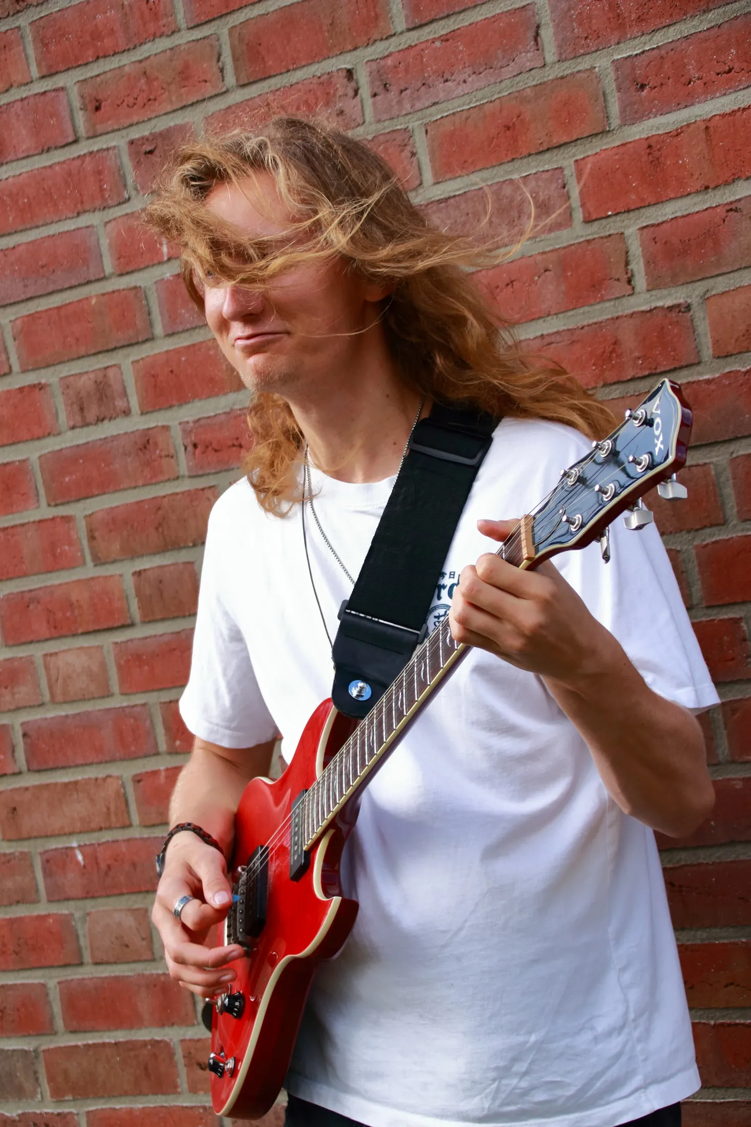 Gitarrist mit roter E-Gitarre vor einer Backsteinwand